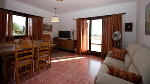 A living room with a sofa, a TV, a dining table with chairs, and a fan. - Sea view, terrace 20 m2, WIFI, parking, barbecue and garden of 1000 m2. (Roses, Girona)