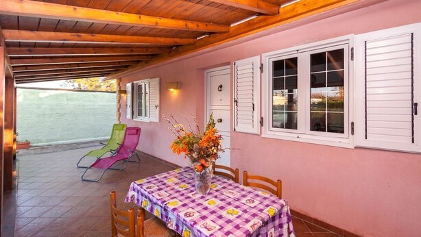 Un patio cubierto con una mesa, sillas, un jarrón de flores y vistas al mar.