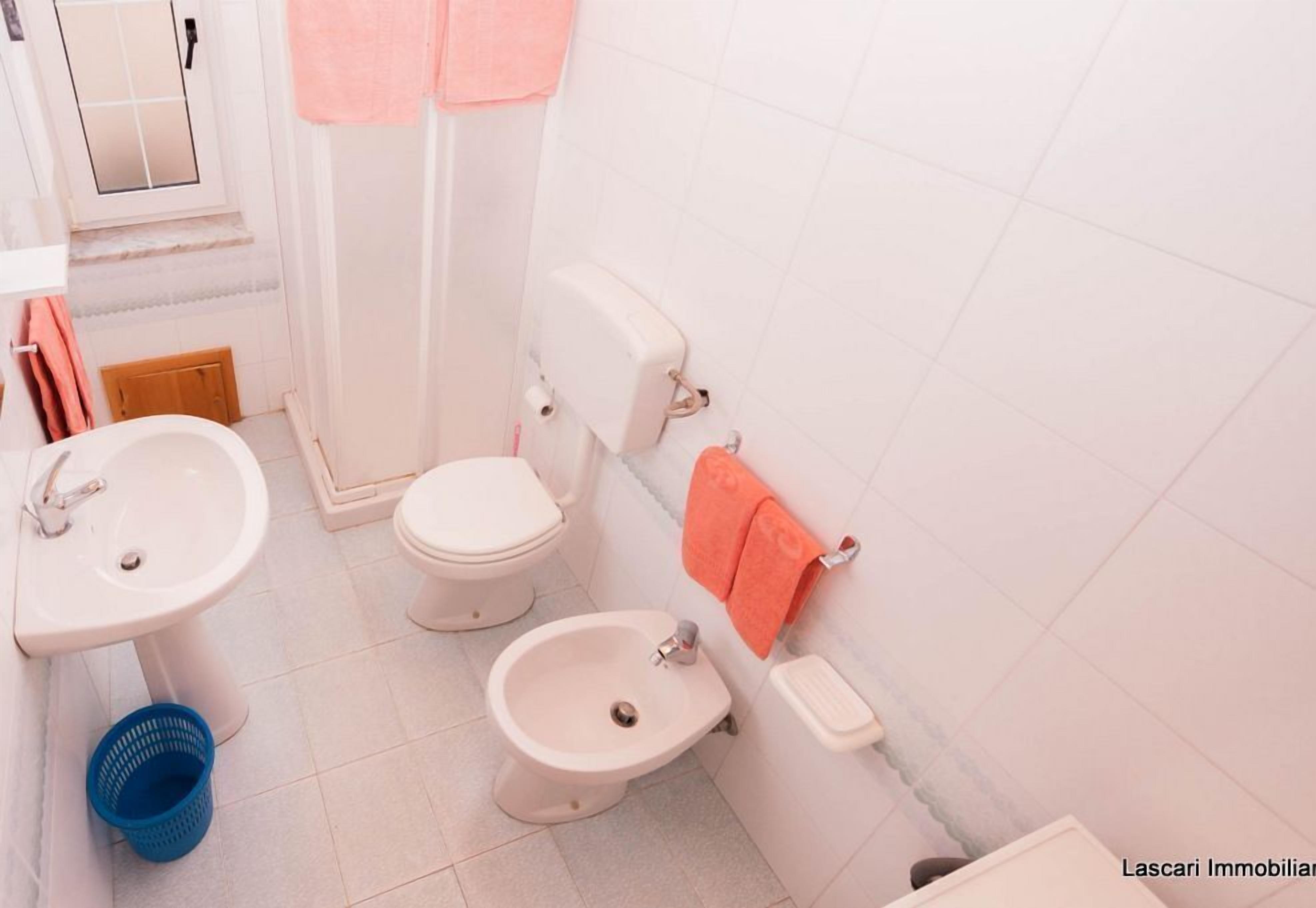 A bathroom with a toilet, bidet, sink, and a blue basket.