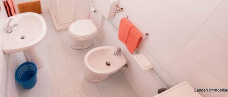 A bathroom with a toilet, bidet, sink, and a blue basket.
