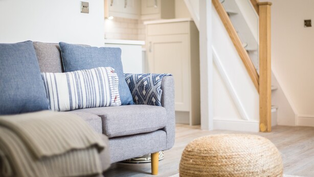 Ein graues Sofa mit gemusterten Kissen in einem Wohnzimmer mit einer Holztreppe und weißen Wänden.