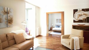 Amplia sala de estar con piso de madera, un sofá color beige y un sillón blanco, además de un ventanal grande.
