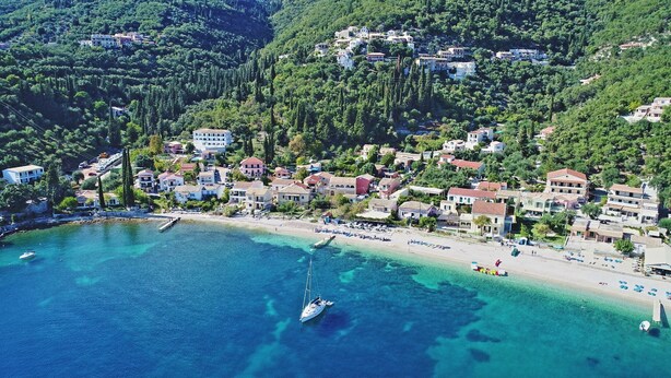 A coastal town with a beach, clear waters, and buildings surrounded by greenery.