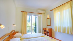 A room with two beds, a wooden desk, a mirror, and a sliding glass door to the outside.