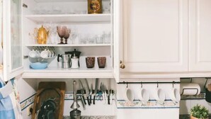 Una cocina con armarios blancos, una cafetera y distintos utensilios de cocina.