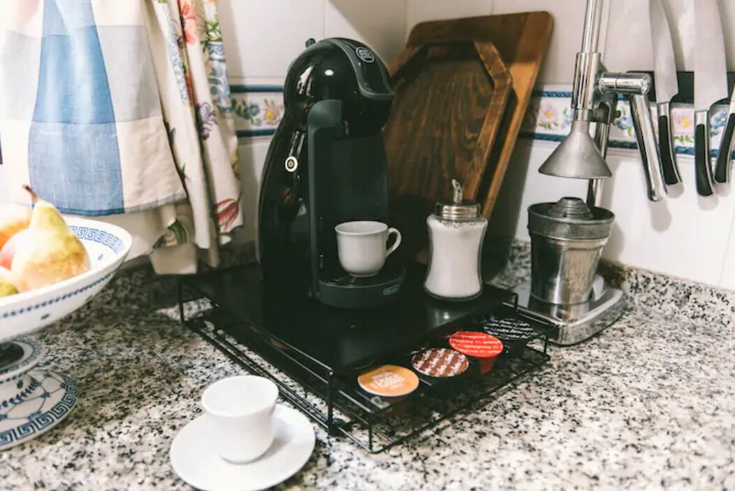 A coffee maker on a kitchen counter with a cup, a sugar container, and a pepper grinder.