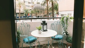 Un balcón con dos sillas y una mesa, con vistas a un paisaje urbano con palmeras y edificios.