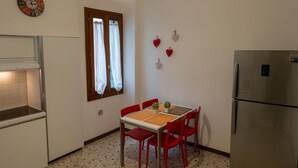 A compact kitchen with a dining table, chairs, a refrigerator, a clock, and a window with curtains. - Ca' Riolfo, Rialto Bridge (Venice)