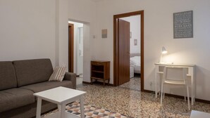 A living room with a sofa, a small white table, a desk with a chair, and a lamp. There is a door leading to another room and a wall with a family rules sign. - Ca' Riolfo, Rialto Bridge (Venice)
