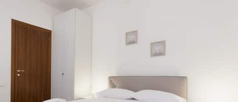 A neatly made bed with white linens, a wooden door, and two small framed pictures on the wall.