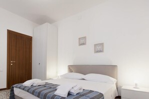 A neatly made bed with white linens, a wooden door, and two small framed pictures on the wall.