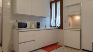 A compact kitchen with white cabinets, a microwave, a coffee maker, and a red mat on the floor.