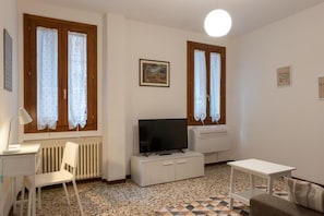 A small, well-lit room with a television on a white cabinet, a radiator, a desk with a chair, and a patterned rug. - Ca' Riolfo, Rialto Bridge (Venice)