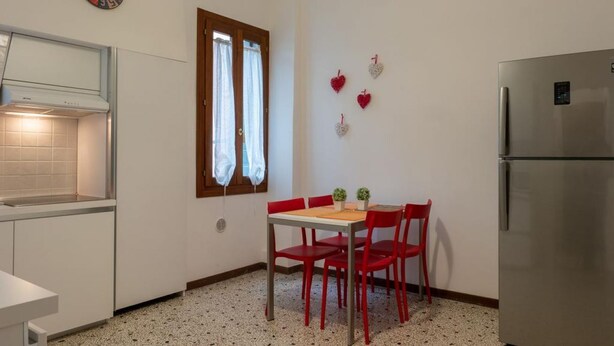 A compact kitchen with a dining table, chairs, a refrigerator, a clock, and a window with curtains. - Ca' Riolfo, Rialto Bridge (Venice)