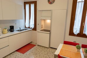 A compact kitchen with white cabinets, a sink, a stove, and a small dining area with a table and chairs. - Ca' Riolfo, Rialto Bridge (Venice)