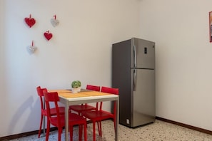 A compact kitchen with a stainless steel refrigerator, a wooden table with red chairs, and decorative heart-shaped ornaments on the wall. - Ca' Riolfo, Rialto Bridge (Venice)