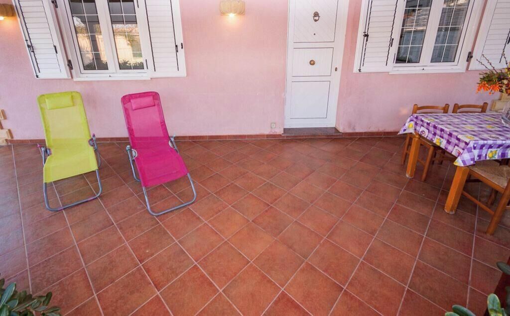 A patio area with two folding chairs, a table with a checkered tablecloth, and a door with a small decorative item above it.