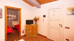 Ein Hotelzimmer mit Holzboden, einem Fernseher auf einer Holzkommode, einer Tür mit einem Hinweis und einer roten Bettdecke.