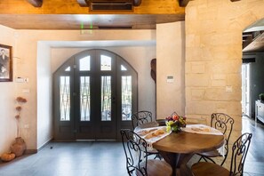 A dining area with a round table, metal chairs, a vase with flowers, and a large arched doorway with windows.