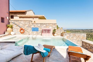 A rooftop infinity pool with a stone wall, a water feature, and lounge chairs.