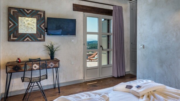 Een slaapkamer met een bed, een bureau met stoel, een televisie en uitzicht op de omgeving.