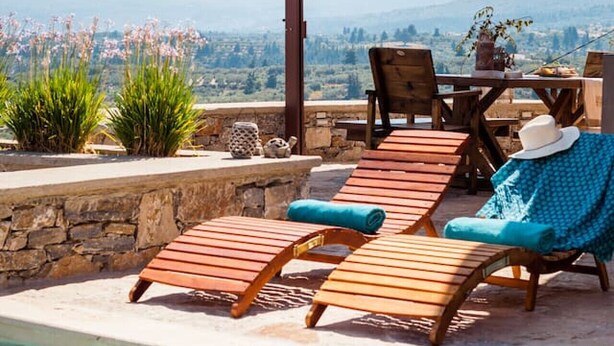 Ein Poolbereich mit Holzliegen, einem Tisch und einem Sonnenschirm.