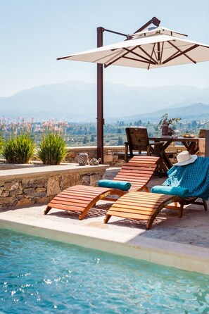A poolside area with wooden loungers, a table, and an umbrella.