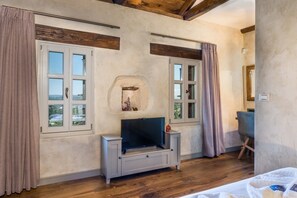 A room with a television, a stone fireplace, and large windows with curtains.