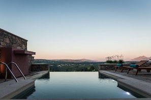 Ein Fernblick auf Berge, Steinmauern und Liegestühle an einem Infinity-Pool.