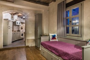 A bedroom with a bed, a window with curtains, a nightstand, and a view into the kitchen.