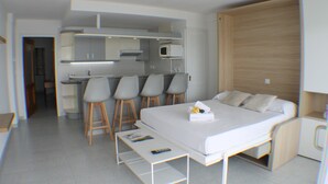 Moderni hotellihuone, jossa on sänky, pieni työpöytä, mikroaaltouuni ja pieni keittiönurkkaus.