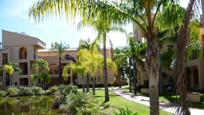 A courtyard with a pond, palm trees, and a building with balconies. - 3-Bedroom Apartment with Sea & Mountain Views (Benahavís)