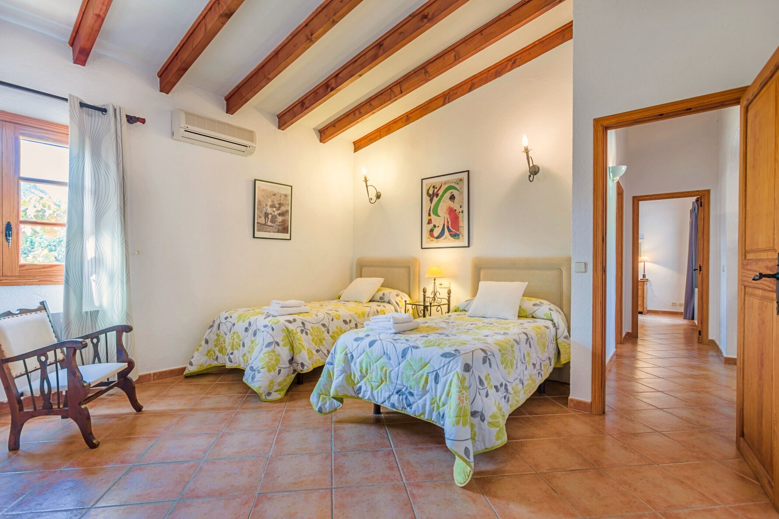 Une chambre avec deux lits, des poutres en bois au plafond, une chaise et une fenêtre avec des rideaux.