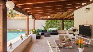 Une terrasse extérieure avec une piscine, un coin salon et une table à manger avec des verres et des assiettes.