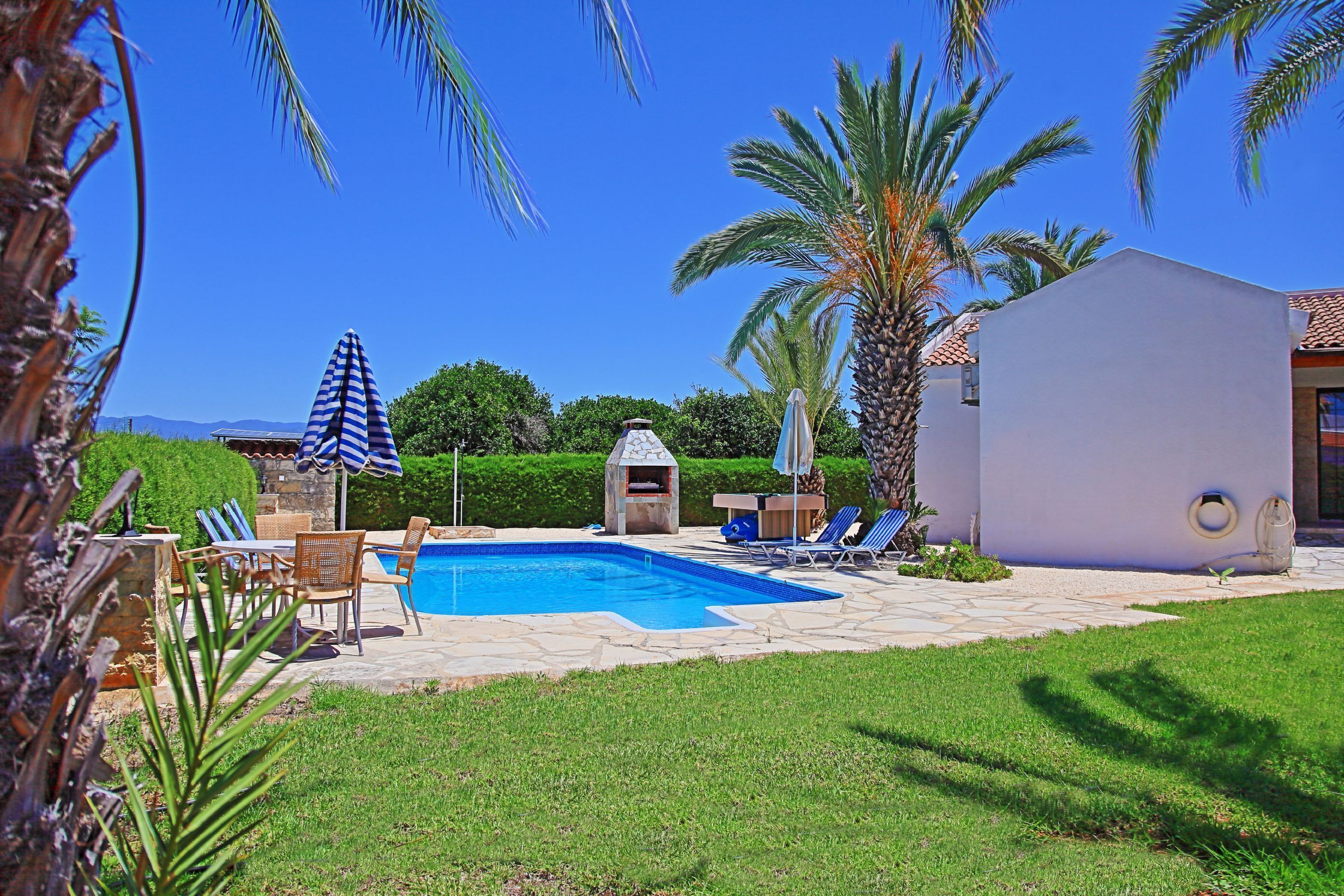 A backyard with a swimming pool, lounge chairs, a barbecue grill, and a small house.