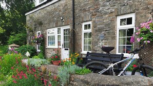 A stone building with a garden in front, a bench, and a bicycle. - Courtyard cottage with extensive private grounds and free WiFi (Swansea)