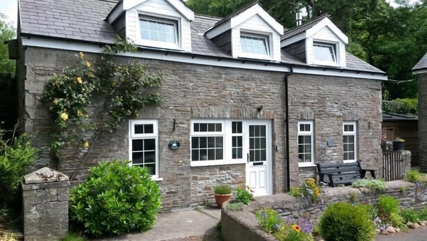 A stone building with a gabled roof, multiple windows, and a small porch area with a bench. - Courtyard cottage with extensive private grounds and free WiFi (Swansea)
