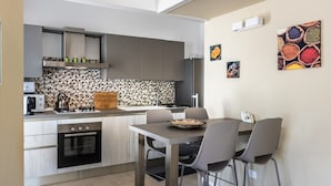 Eine kompakte Küche mit Essbereich, mit modernem Design, grauen Schränken, einer gefliesten Spritzschutzwand und einem kleinen Esstisch mit Stühlen.