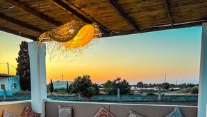 An outdoor seating area with a bench and cushions, overlooking a scenic landscape during sunset.