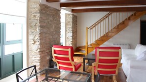 A room with a stone wall, wooden staircase, red striped chairs, a white sofa, and a glass table.