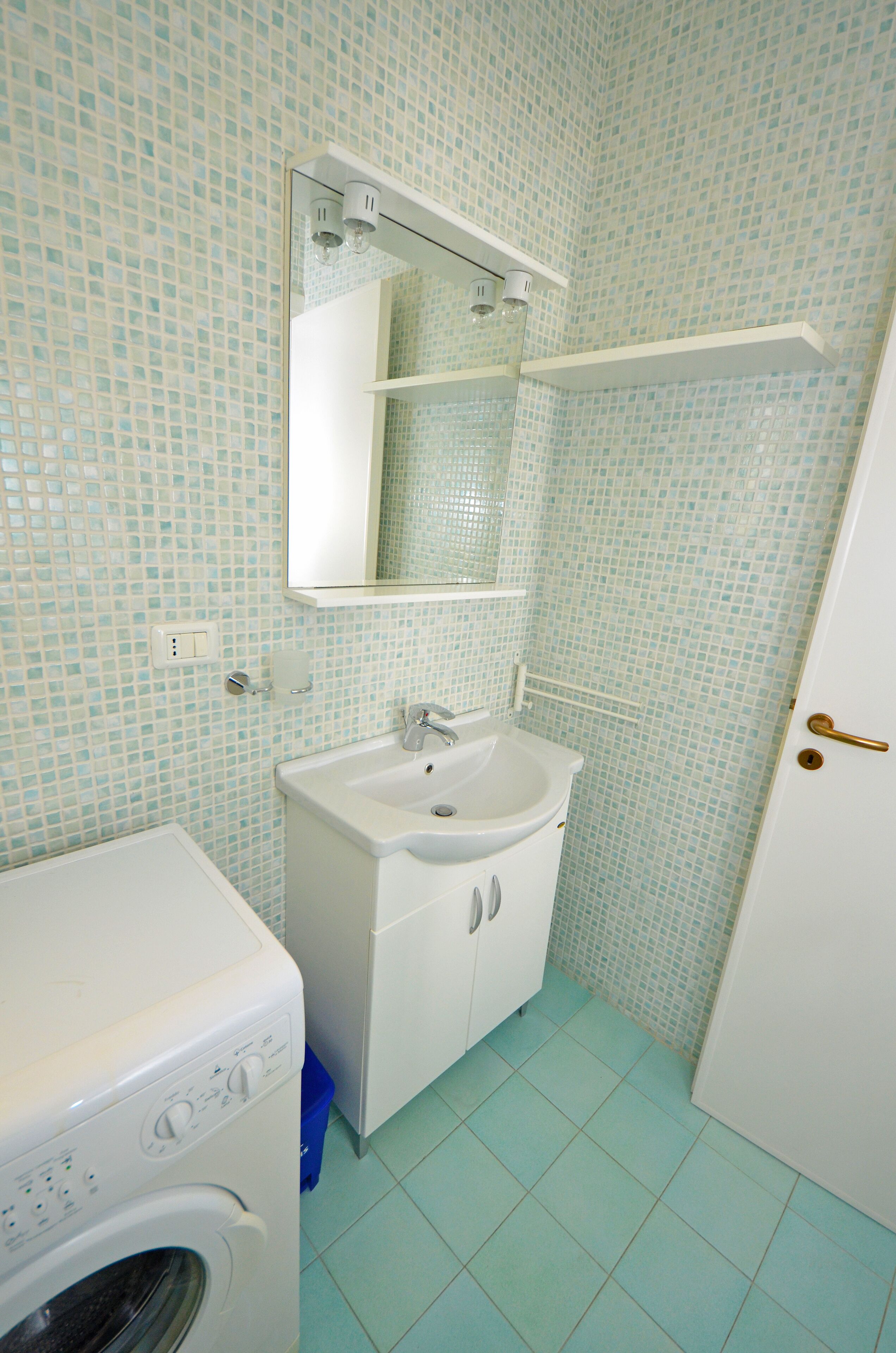 Uma casa de banho pequena com máquina de lavar roupa, lavatório e espelho.