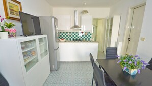 Una cocina compacta con armarios blancos, salpicadero de azulejos, un refrigerador y una mesa de comedor con sillas.
