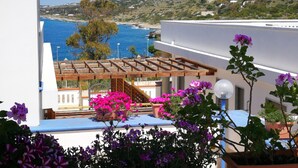 Una terraza en la azotea con vista al mar, plantas en macetas y una pérgola de madera.