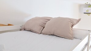 A bed with two pillows and a white mattress in a room with white walls and an air conditioning unit on the wall.