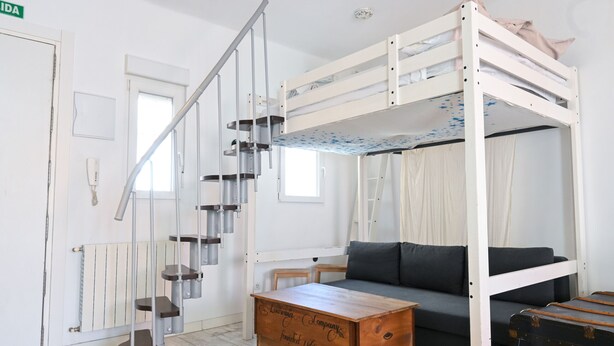 A bunk bed with a ladder, a sofa, a wooden chest, and a suitcase.