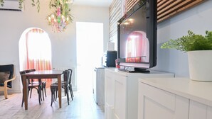A modern kitchen with white cabinets, a dining area with a wooden table and chairs, and a TV mounted on the wall.