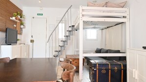 A bunk bed with a desk and chairs, a wooden wall with shelves, a suitcase, and a television.