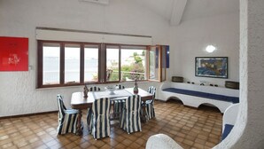 A dining area with a large window, a table with chairs, and a bench along the wall. - Independent villa on the sea (Isola)
