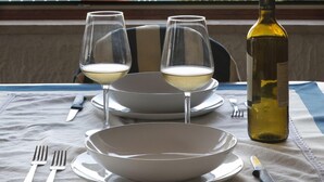 A table set with two wine glasses, a bottle of wine, and plates on a balcony overlooking a coastal cityscape. - Independent villa on the sea (Isola)