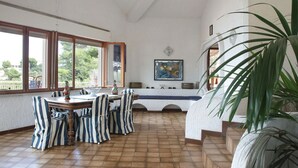 A dining area with a wooden table and striped chairs, a large window with a view of greenery, and a painting on the wall. - Independent villa on the sea (Isola)
